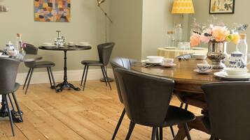 A dining area with a round wooden table, black chairs, and a small round table with a lamp.