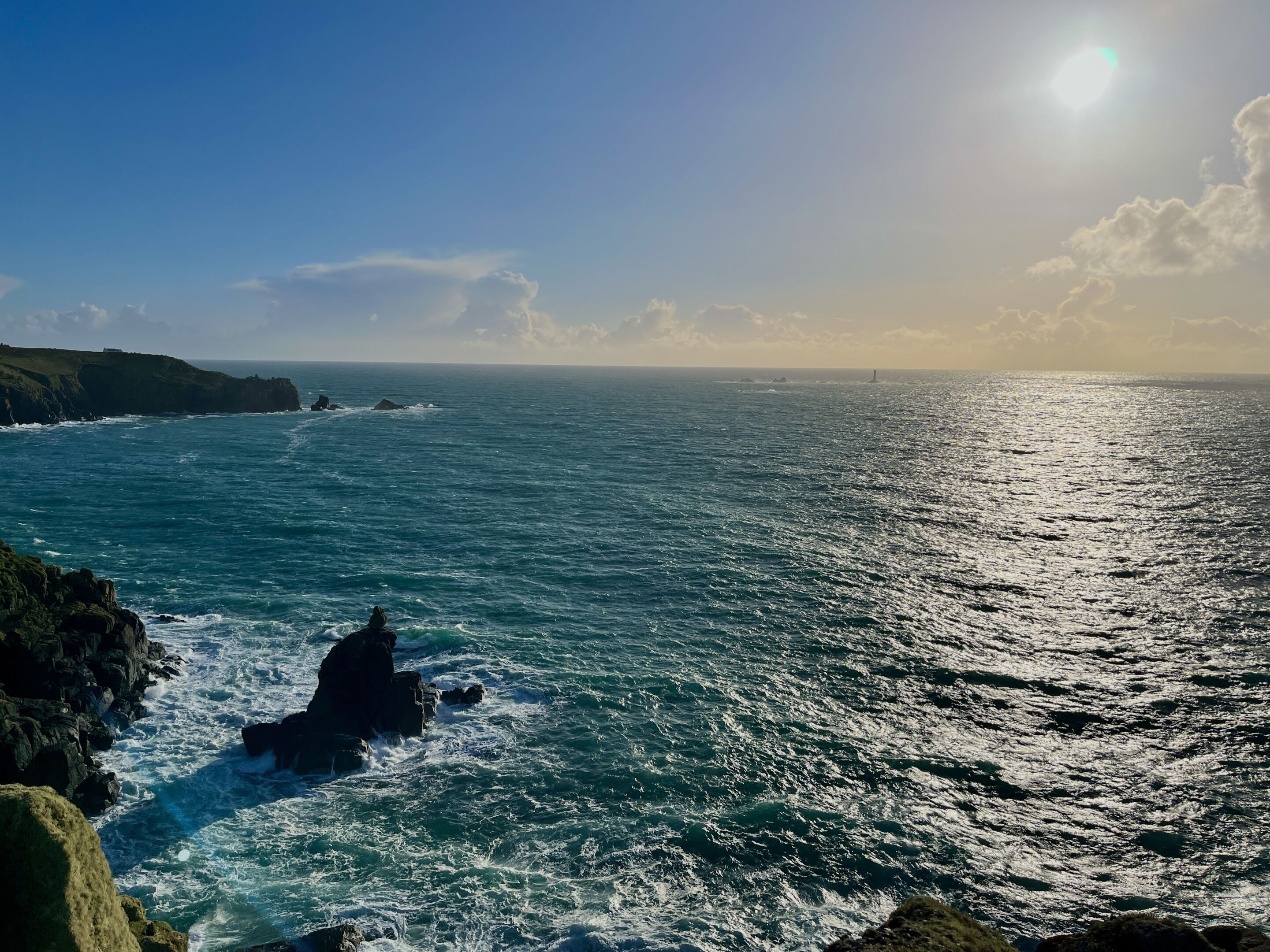 A coastal landscape with a rocky shoreline, waves crashing against the rocks, and a clear sky.