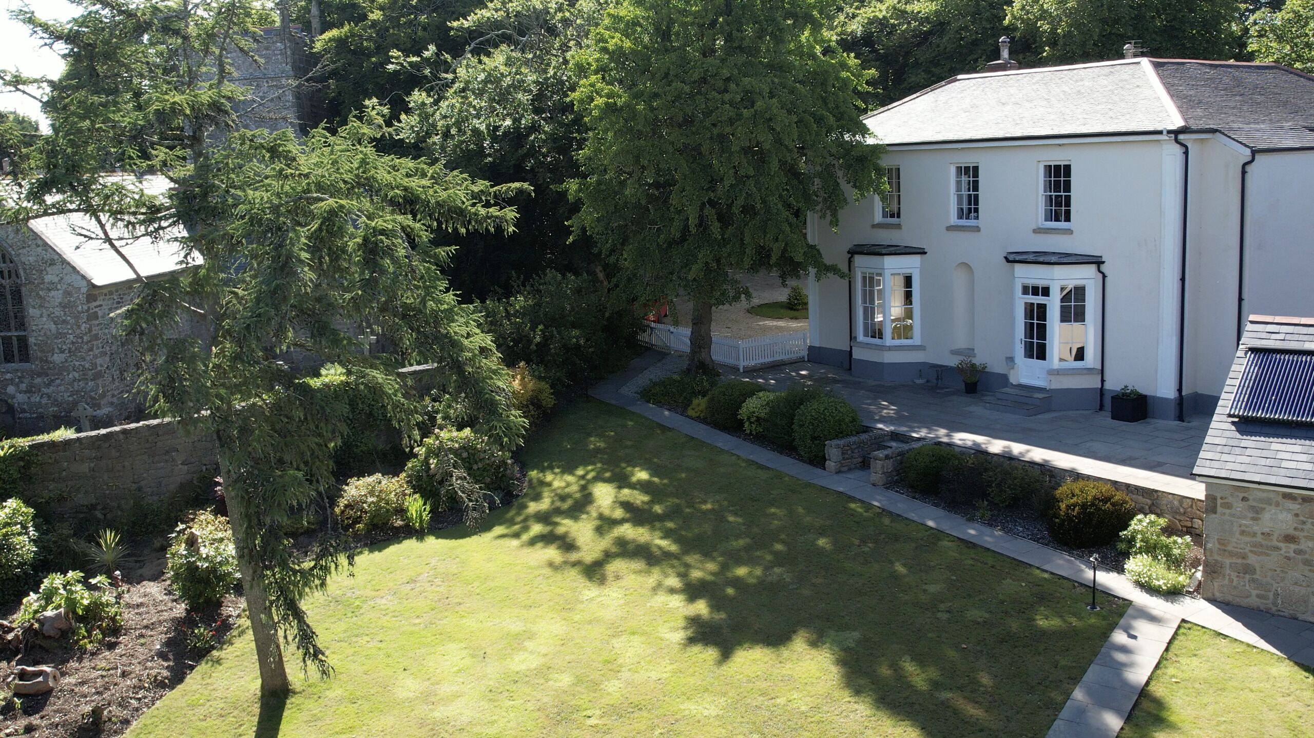 A white house with a well-maintained lawn, a stone wall, and a large tree.
