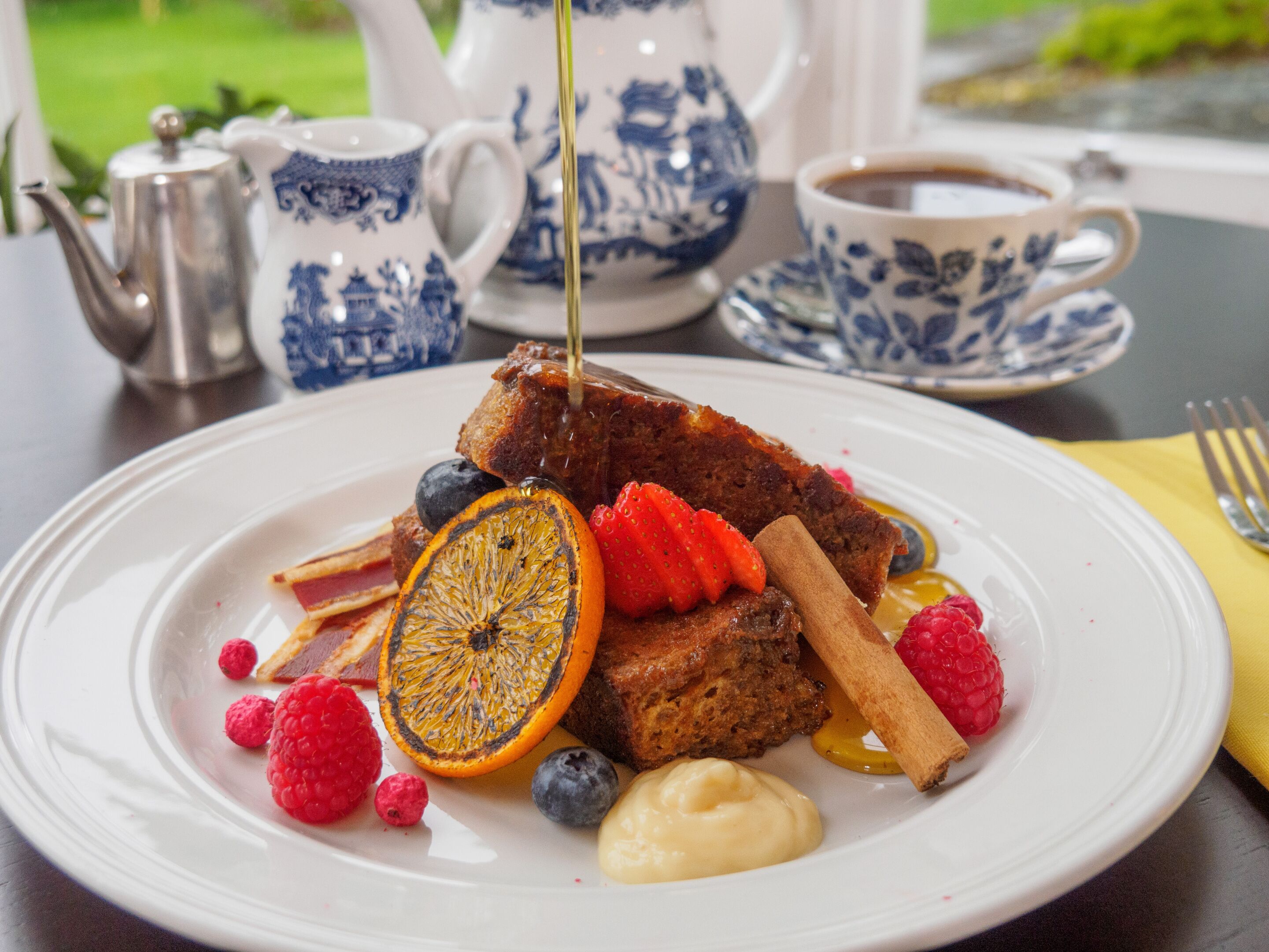 A breakfast plate with toast, fruit, and syrup, accompanied by a teapot and cup on a table.