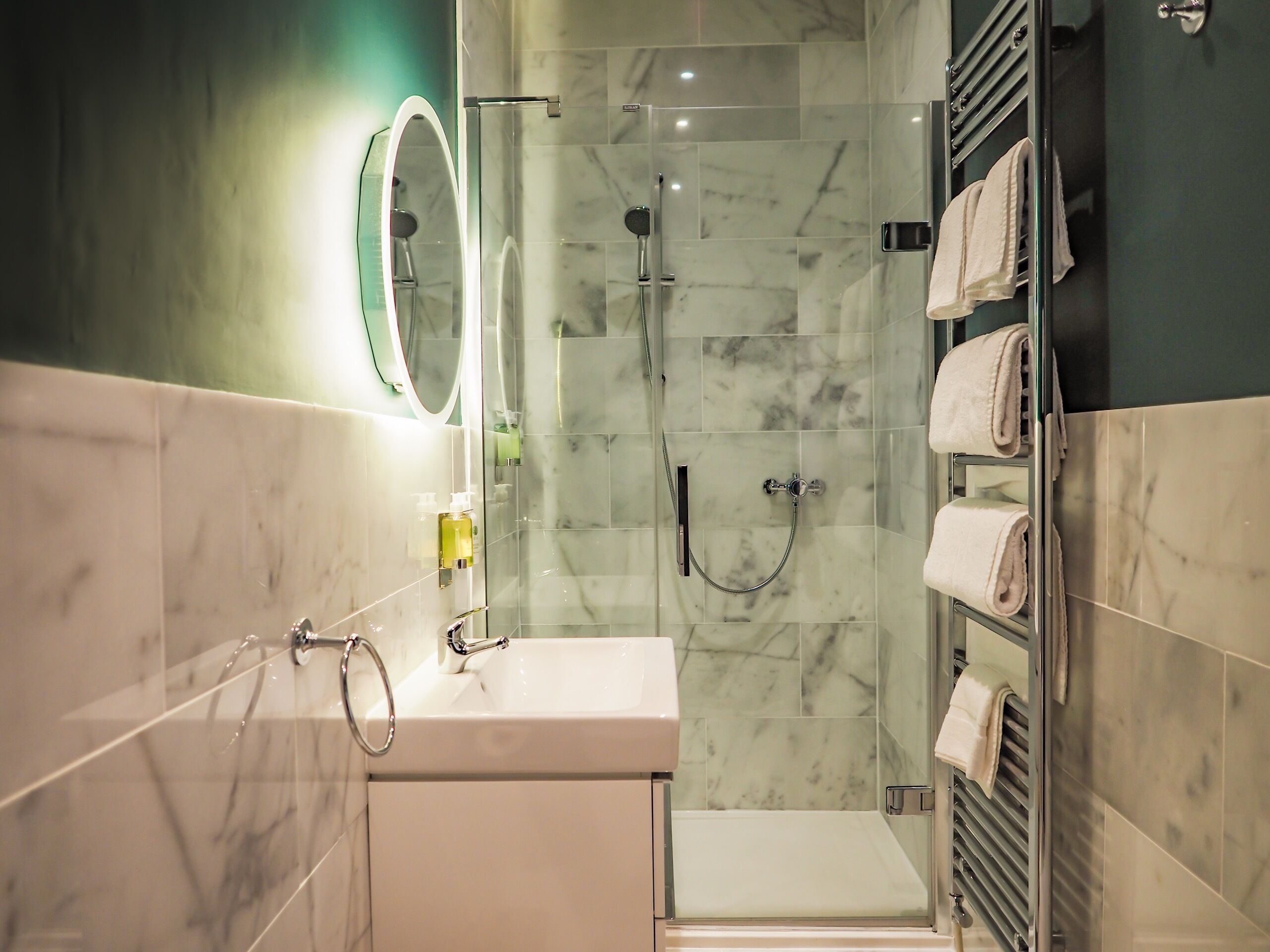 A modern bathroom with a glass-enclosed shower, a sink with a mirror, and a towel rack with neatly folded towels.