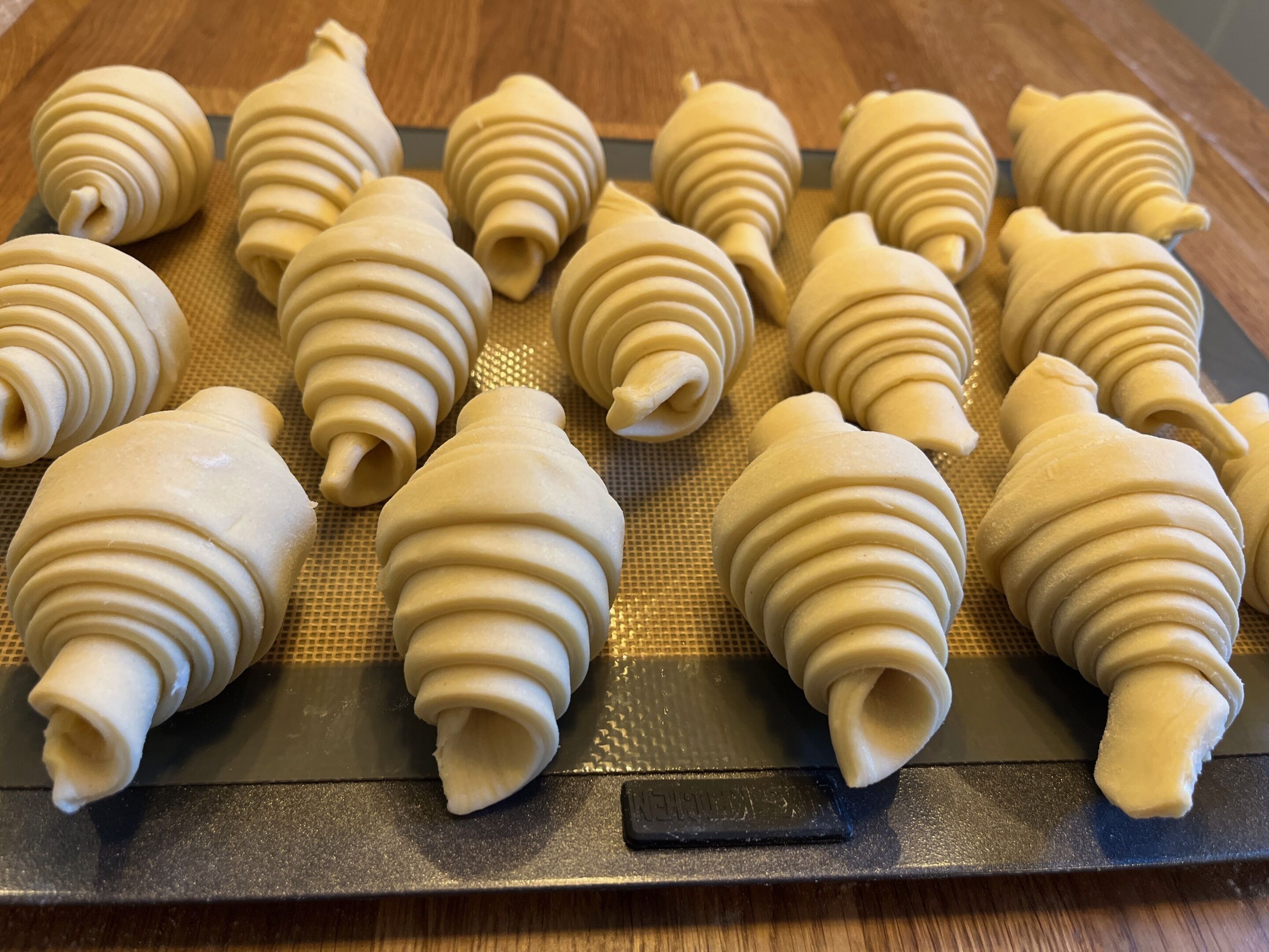 A tray of dough shaped into spirals on a baking mat.