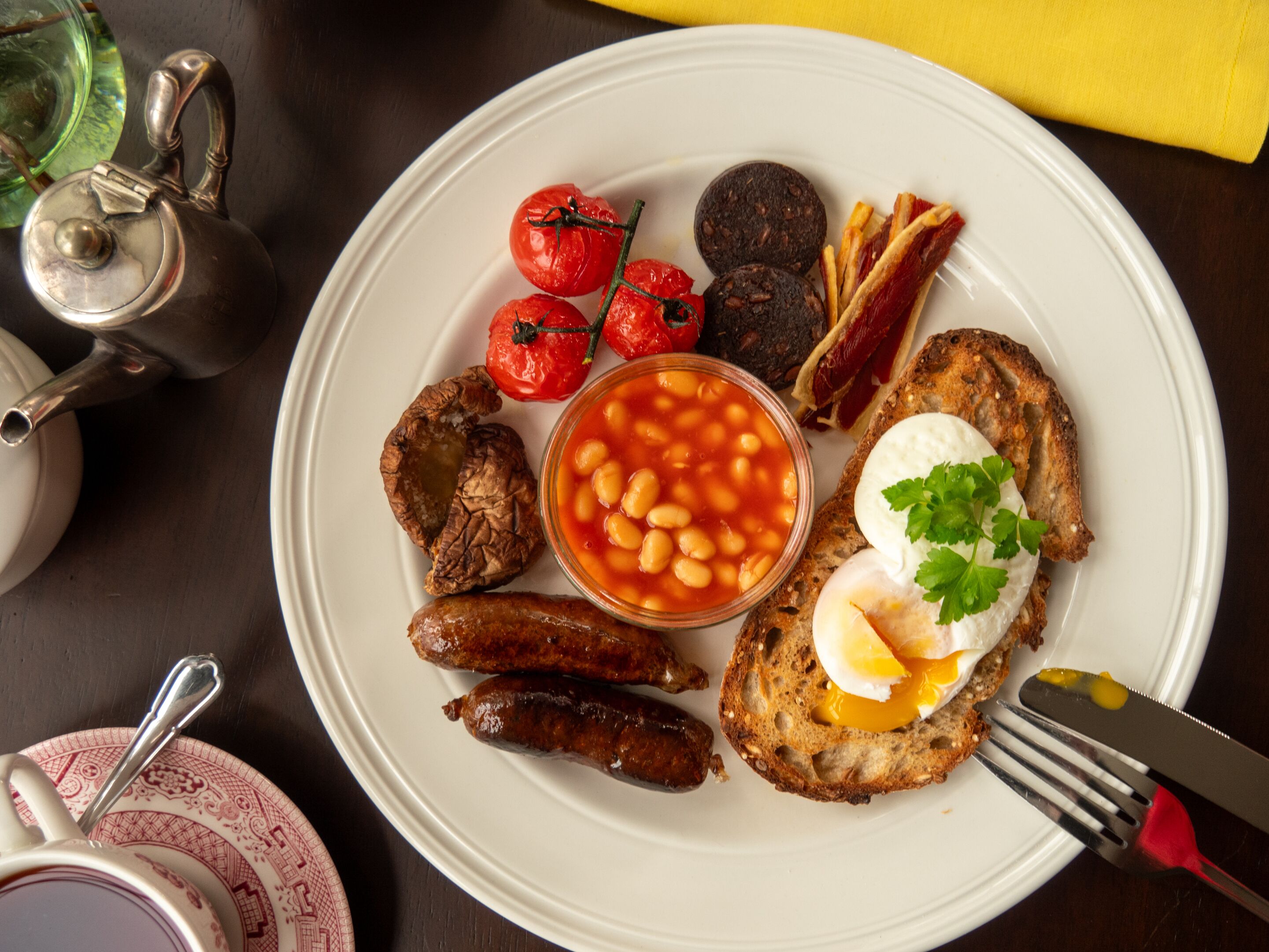 A plate of breakfast food including sausages, beans, tomatoes, and toast with a poached egg.