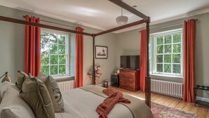 Una cama con dosel de madera, un televisor sobre un mueble de madera y una ventana con cortinas rojas.