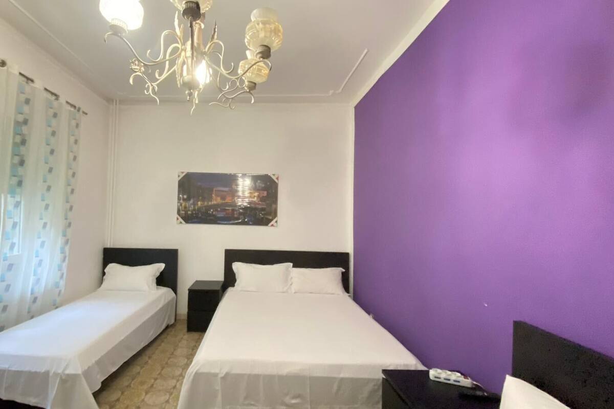 A hotel room with two single beds, a chandelier, a cityscape painting, and a purple accent wall.