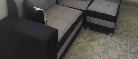 Un sofá modular con una paleta de colores en negro y gris, ubicado frente a una pared con una ventana y cortinas naranjas.