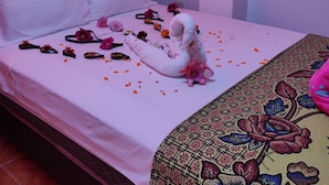 Un letto rifatto con cura, con lenzuola bianche, un cigno decorativo e petali di fiori sparsi.