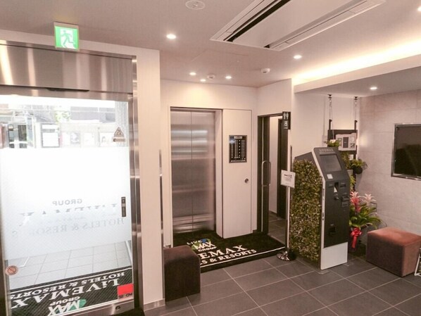 A hotel lobby with a reception desk, an elevator, and a self-service kiosk. - HOTEL LiVEMAX Tokyo Kanda-Ekimae (Tokyo)