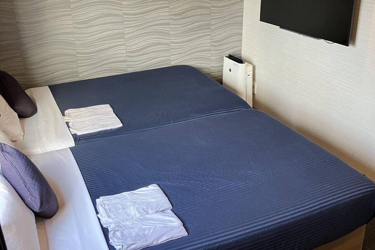 A hotel room with a bed, a flat-screen TV mounted on the wall, and a small bedside table.