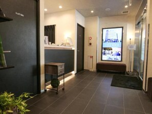 A hotel lobby with a reception desk, a bench, a plant, and a large window with a view of a building. - HOTEL LiVEMAX Tokyo Kanda-Ekimae (Tokyo)