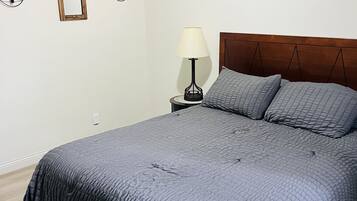 Relax in a serene bedroom with a large bed, wooden headboard, and a bedside table with a lamp and potted plant.