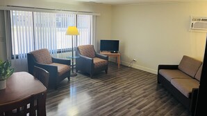 Ein Wohnzimmer mit Holzboden, zwei Sesseln, einem Sofa, einem kleinen Tisch, einer Lampe und einem Fernseher.