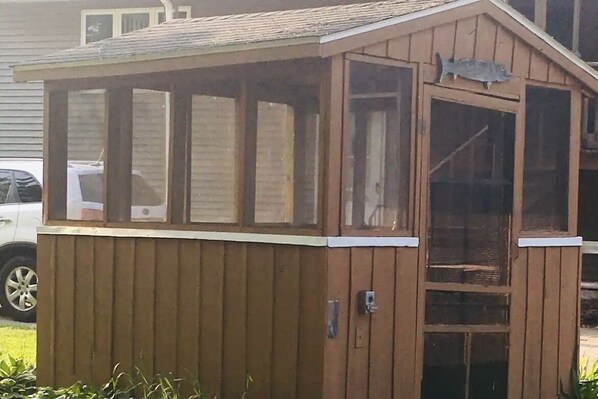 A wooden shed with a door and windows, a metal latch, and a fish symbol on the door.