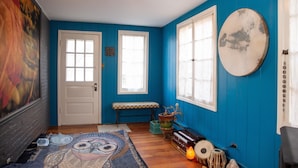 Een kamer met blauwe wanden, een houten vloer, een bankje, een vloerkleed, een deur en een groot schilderij.