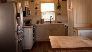Een keuken met witte kastjes, een roestvrijstalen koelkast, een houten tafel en een raam met decoratief roedeverdeling.