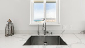 A modern kitchen with a stainless steel sink, a window with a view of the sea, and a metal grater on the counter. - Point Arena Lighthouse - Head Keeper's House (Point Arena)