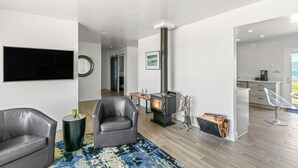 A modern living room with a fireplace, leather sofas, a flat-screen TV, and a kitchen area in the background. - Point Arena Lighthouse - Head Keeper's House (Point Arena)