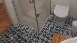 A glass-enclosed shower with a handheld showerhead, a toilet, and a patterned floor.