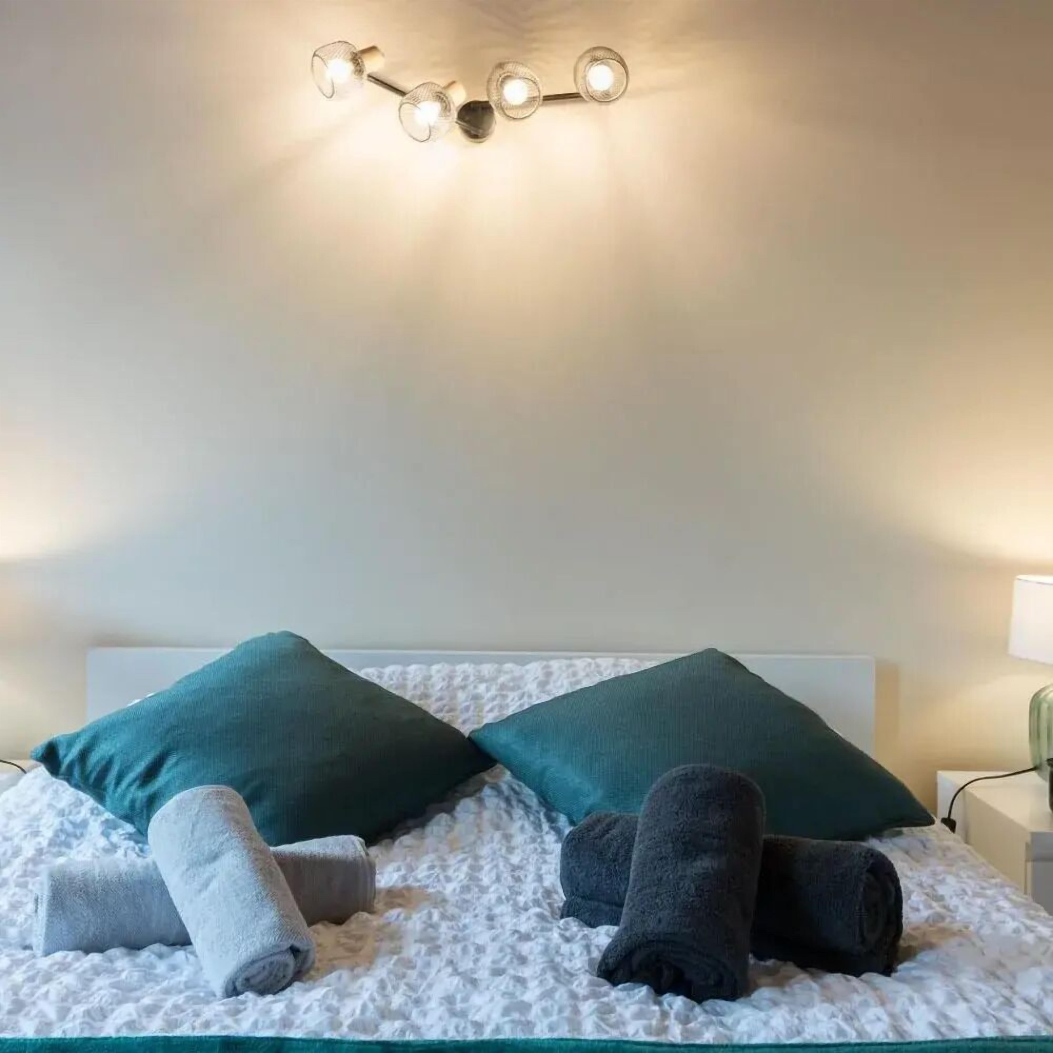 Una cama bien hecha con dos almohadas, una manta blanca texturizada y dos toallas enrolladas.