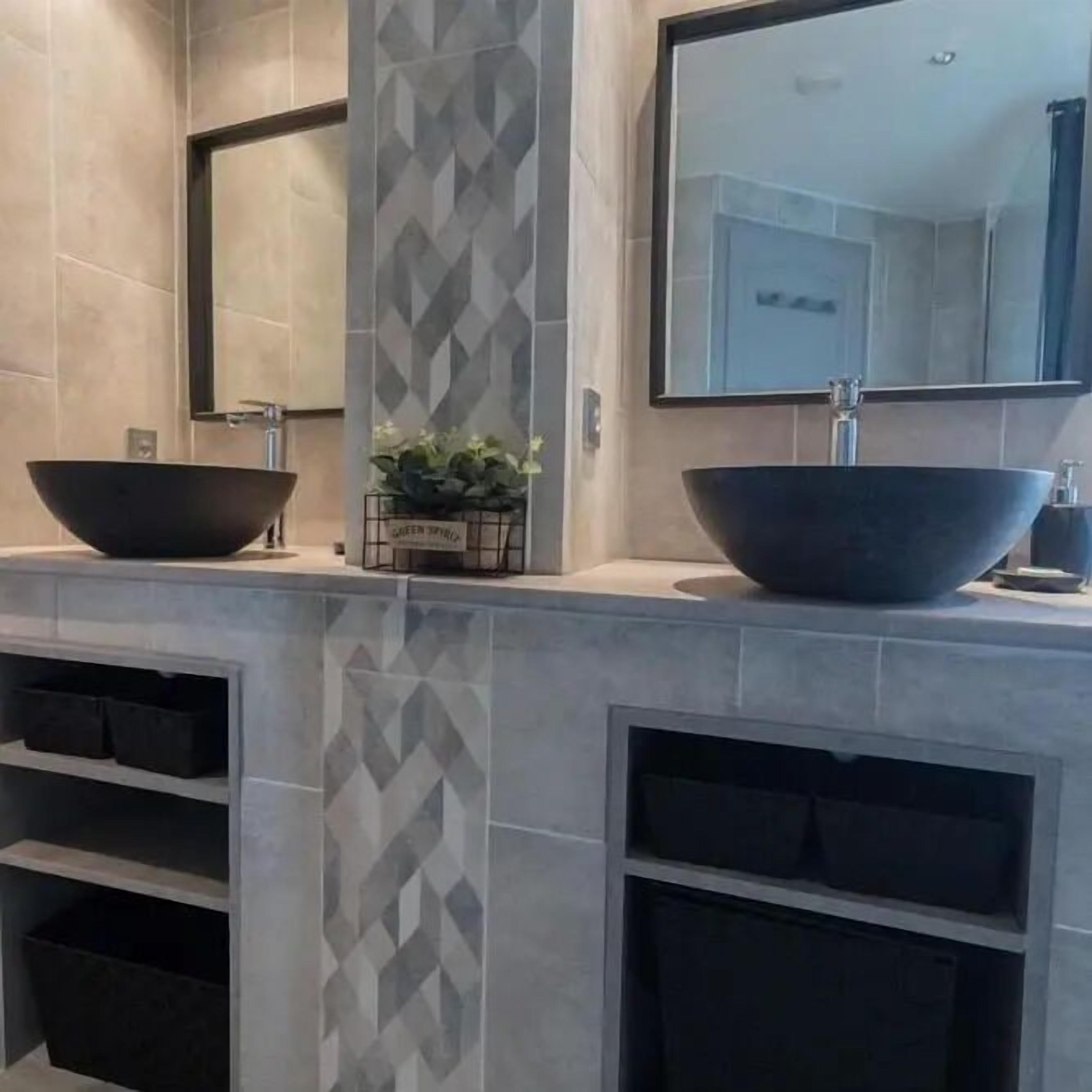 A bathroom with two large black vessel sinks, a mirror above each sink, and a geometric patterned tile backsplash.