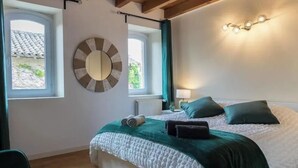 Een slaapkamer met een bed, twee ramen, een spiegel en een wandlamp.