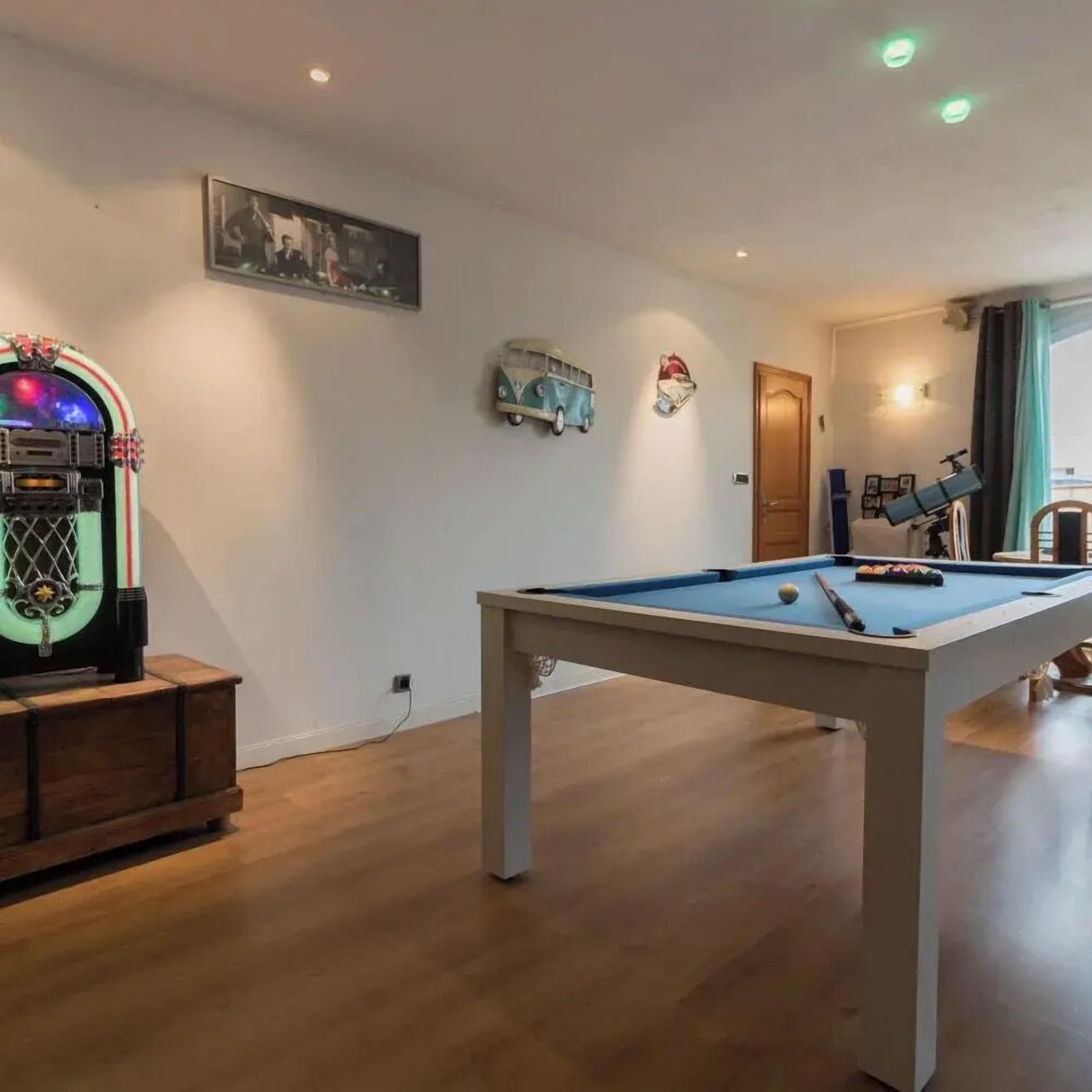 Een pooltafel in een ruimte met houten vloeren, een vintage jukebox en een telescoop op een tafel.