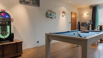 Een pooltafel in een ruimte met houten vloeren, een vintage jukebox en een telescoop op een tafel.