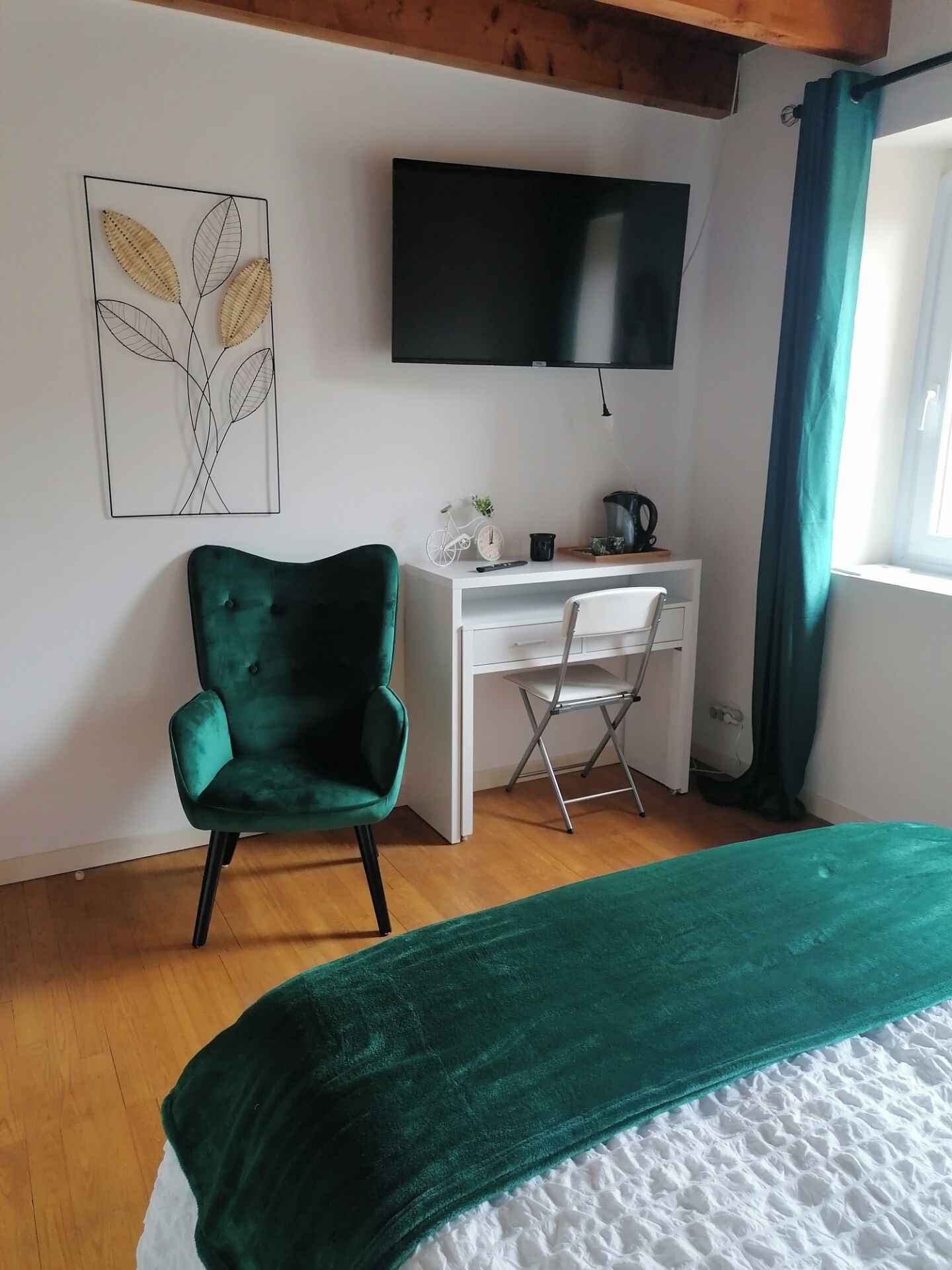 Un dormitorio con cama, escritorio, silla, televisor y ventana con cortinas.