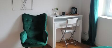 Une chambre à coucher comprenant un lit, un bureau, une chaise, un téléviseur et une fenêtre avec des rideaux.