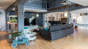 Een ruime woonkamer met een grote televisie, een pooltafel en een moderne bank.