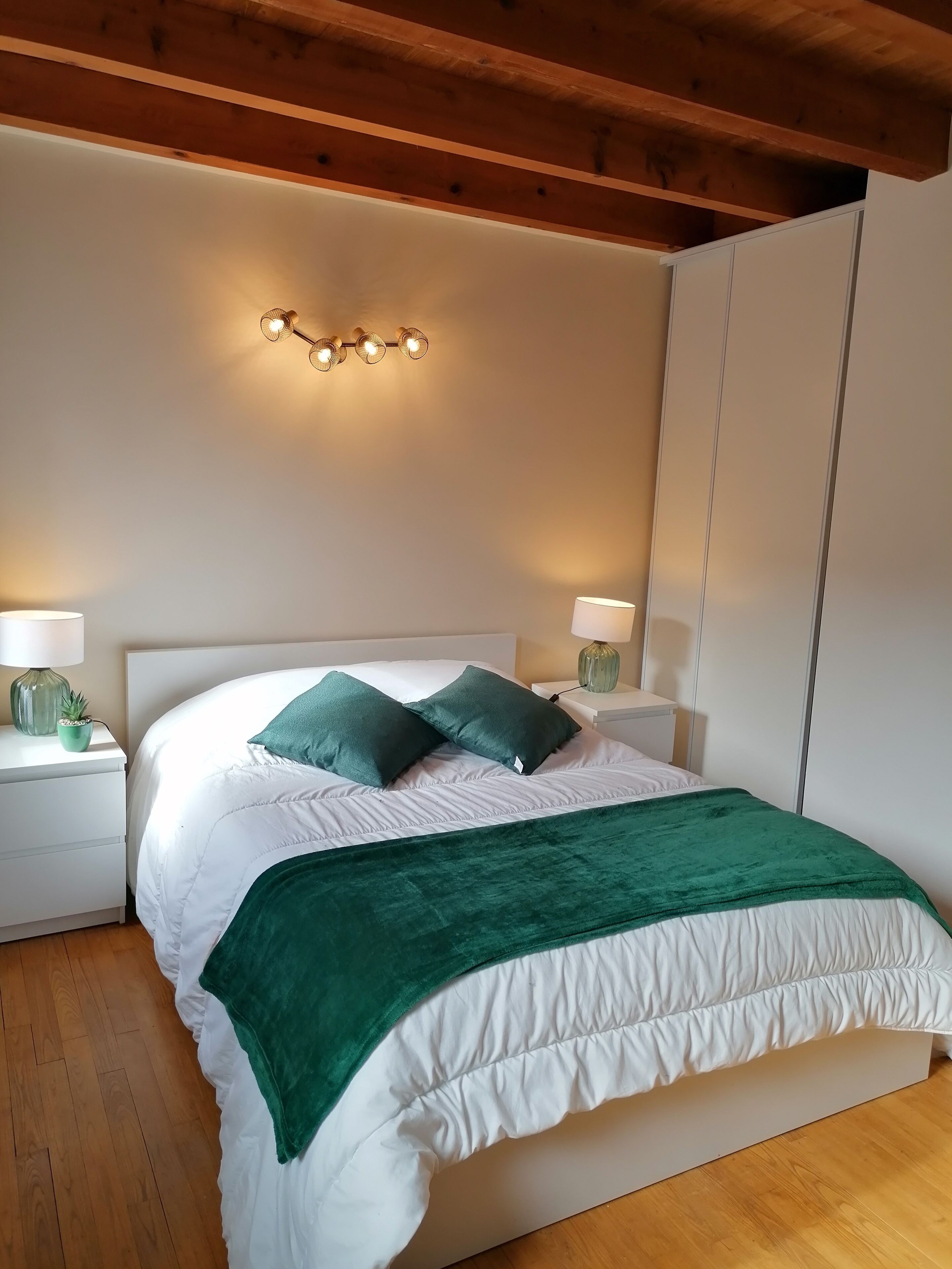Un dormitorio ordenado con cama, dos mesitas de noche con lámparas, un aplique de pared y un armario.