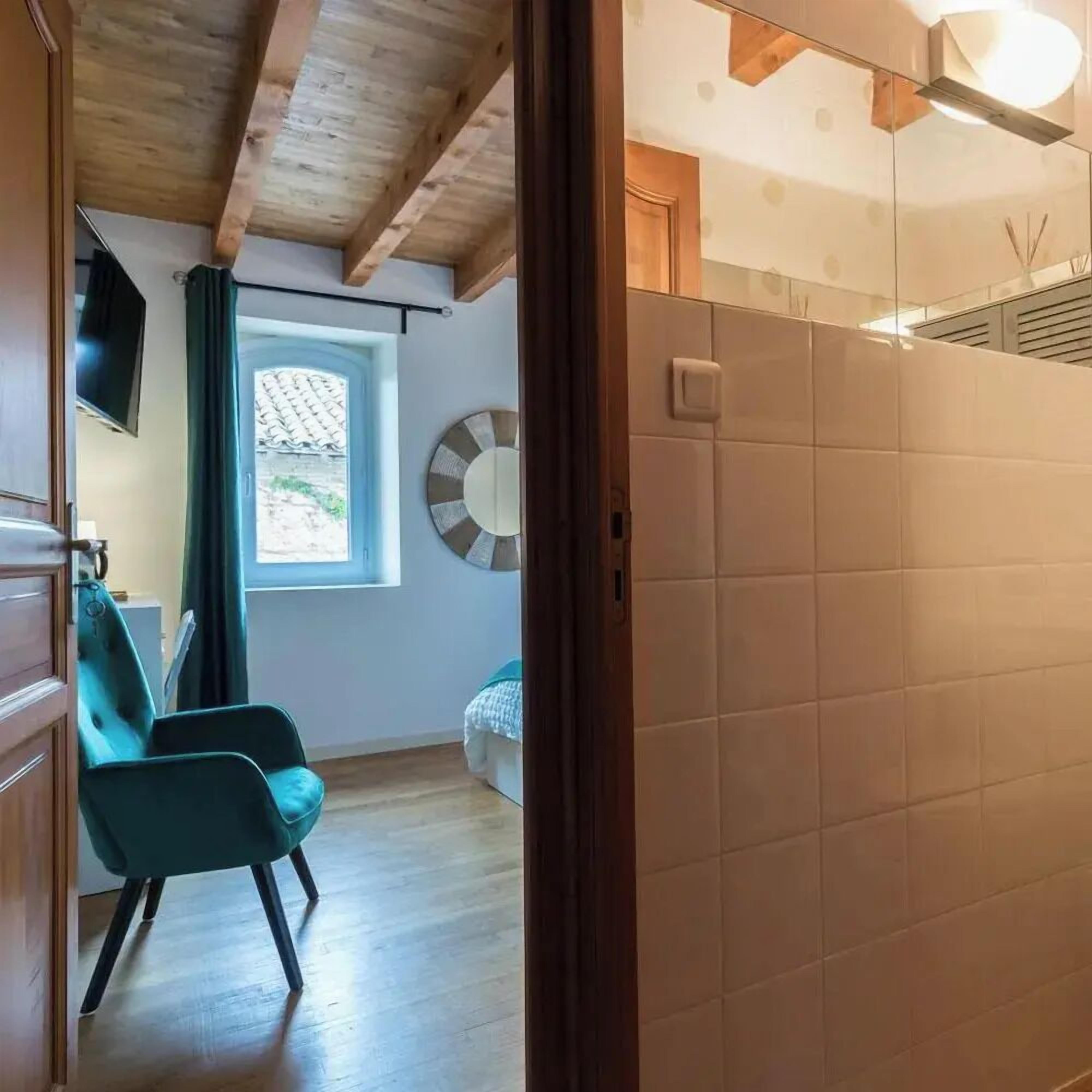Quarto com teto de madeira, janela com vista, uma cadeira e parede com decoração circular.