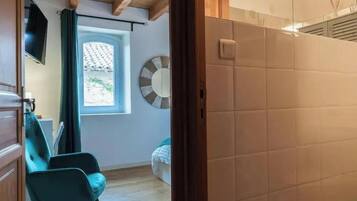Quarto com teto de madeira, janela com vista, uma cadeira e parede com decoração circular.