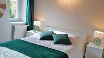 A bedroom with a large bed, two bedside tables with lamps, a window with curtains, and a ceiling light fixture.