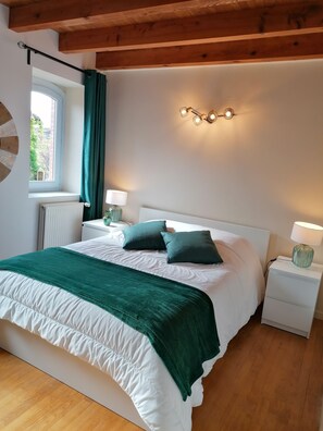 Ein Schlafzimmer mit einem großen Bett, zwei Nachttischen inklusive Lampen, einem Fenster mit Vorhängen und einer Deckenleuchte.