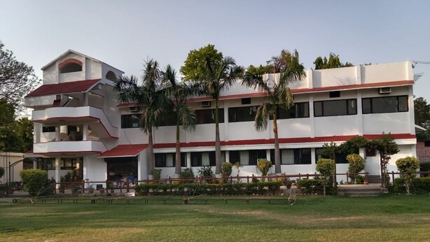 A multi-story building with a flat roof, surrounded by a well-maintained lawn and palm trees. - Avexia Fun City Resort  (Mirzapur)