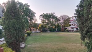 A grassy courtyard with trees and a building in the background. - Avexia Fun City Resort  (Mirzapur)