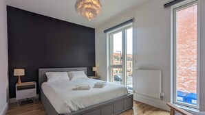 Une chambre à coucher moderne avec un grand lit, des lampes de chevet, un radiateur et une vue sur l’extérieur.