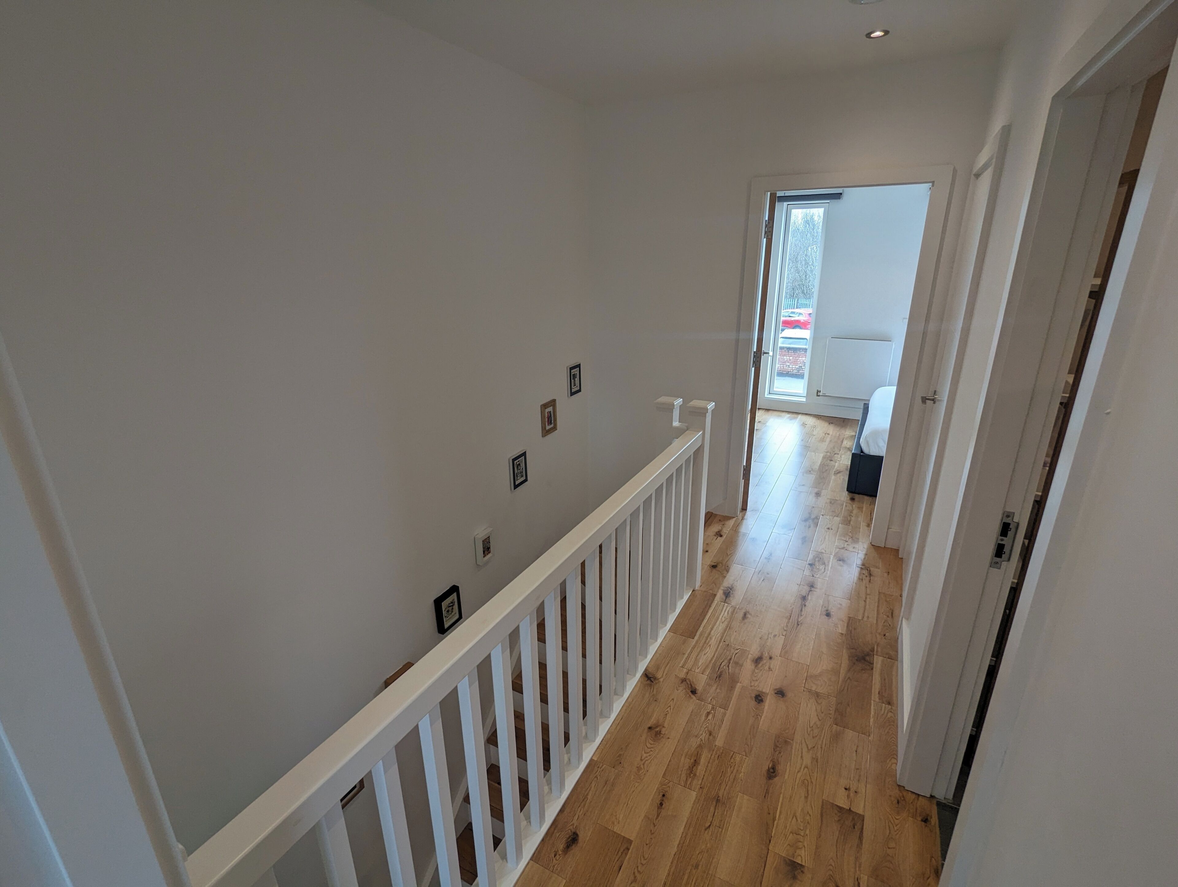 Un couloir doté d’un plancher en bois, de murs blancs et d’une rambarde blanche.
