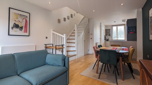 Un interior moderno con un sofá azul, una zona de comedor y una escalera.