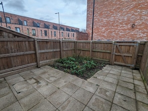 Een binnenplaats met een houten omheining, een bakstenen gebouw en een verharde vloer.