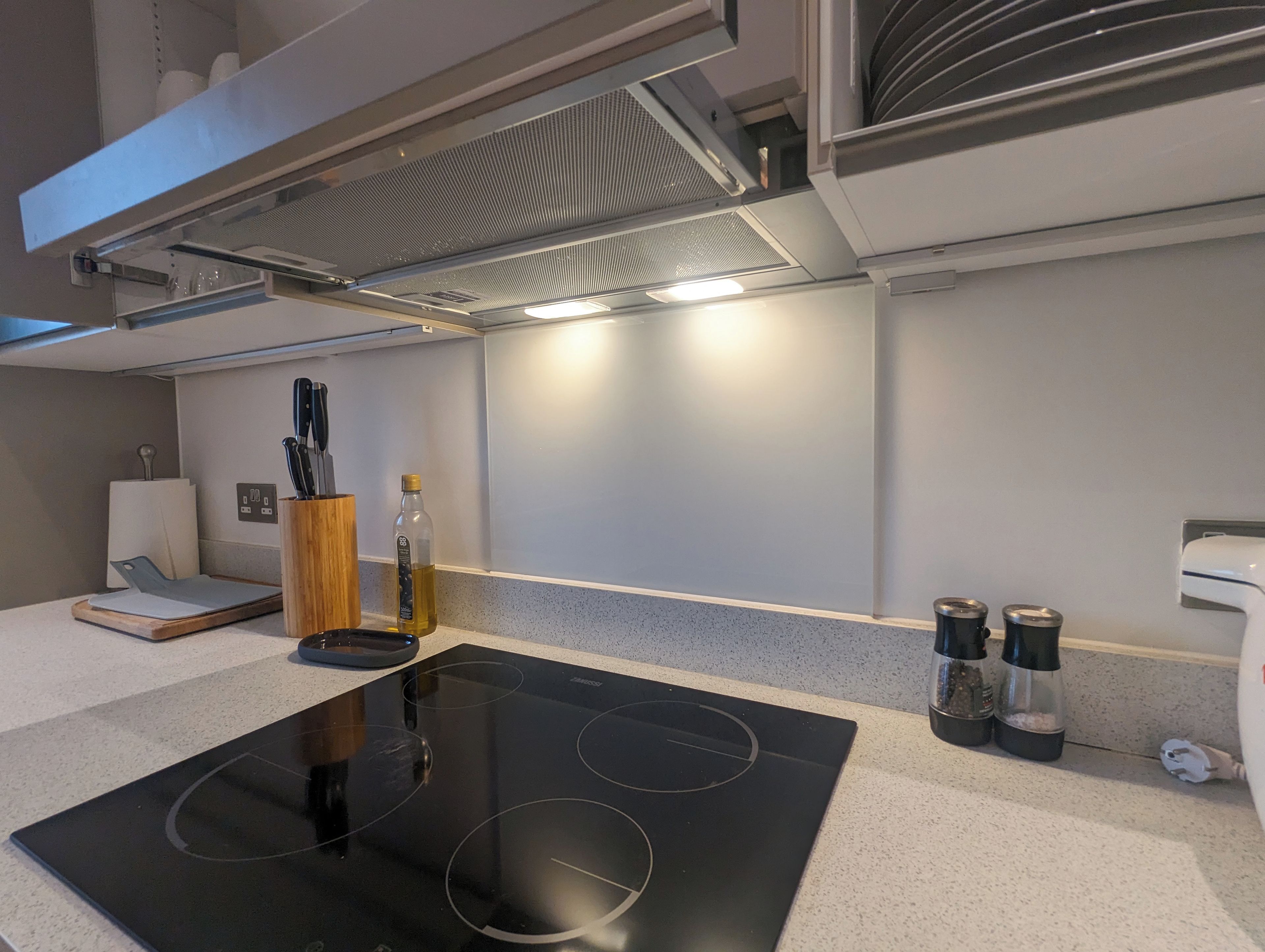 A modern kitchen with a black induction cooktop, a wooden cutting board, a knife block, a bottle of oil, and a coffee maker.