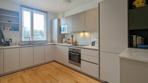 Une cuisine moderne dotée d’appareils électroménagers intégrés, d’une fenêtre avec stores et d’un plancher en bois.