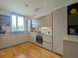 Een moderne keuken met inbouwapparatuur, een raam met zonwering en een houten vloer.