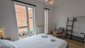 Una habitación de hotel con una cama grande, dos ventanas, una silla, un calentador portátil y una escalera.