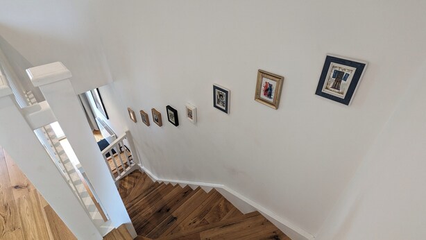 Un escalier avec des marches en bois menant à un palier aux murs blancs, orné de tableaux encadrés.