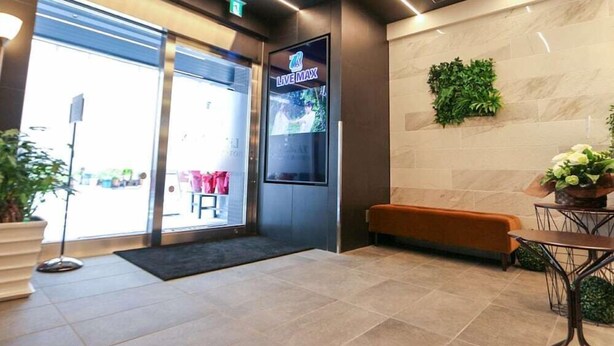 A modern lobby with a reception desk, a bench, and a wall-mounted TV displaying 'LIVE MAX'. - HOTEL LiVEMAX Nihonbashi-Ningyocho (Tokyo)