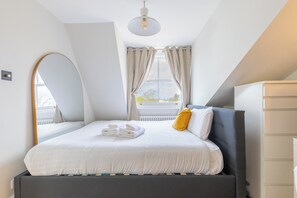 A modern bedroom with a bed, a bedside table, a mirror, and a window with curtains. - 2BDR Hidden Gem in the Heart of Clapham (London)