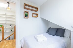 A bedroom with a bed, pillows, a towel, a wooden shelf with a plant, and a staircase. - 2BDR Hidden Gem in the Heart of Clapham (London)