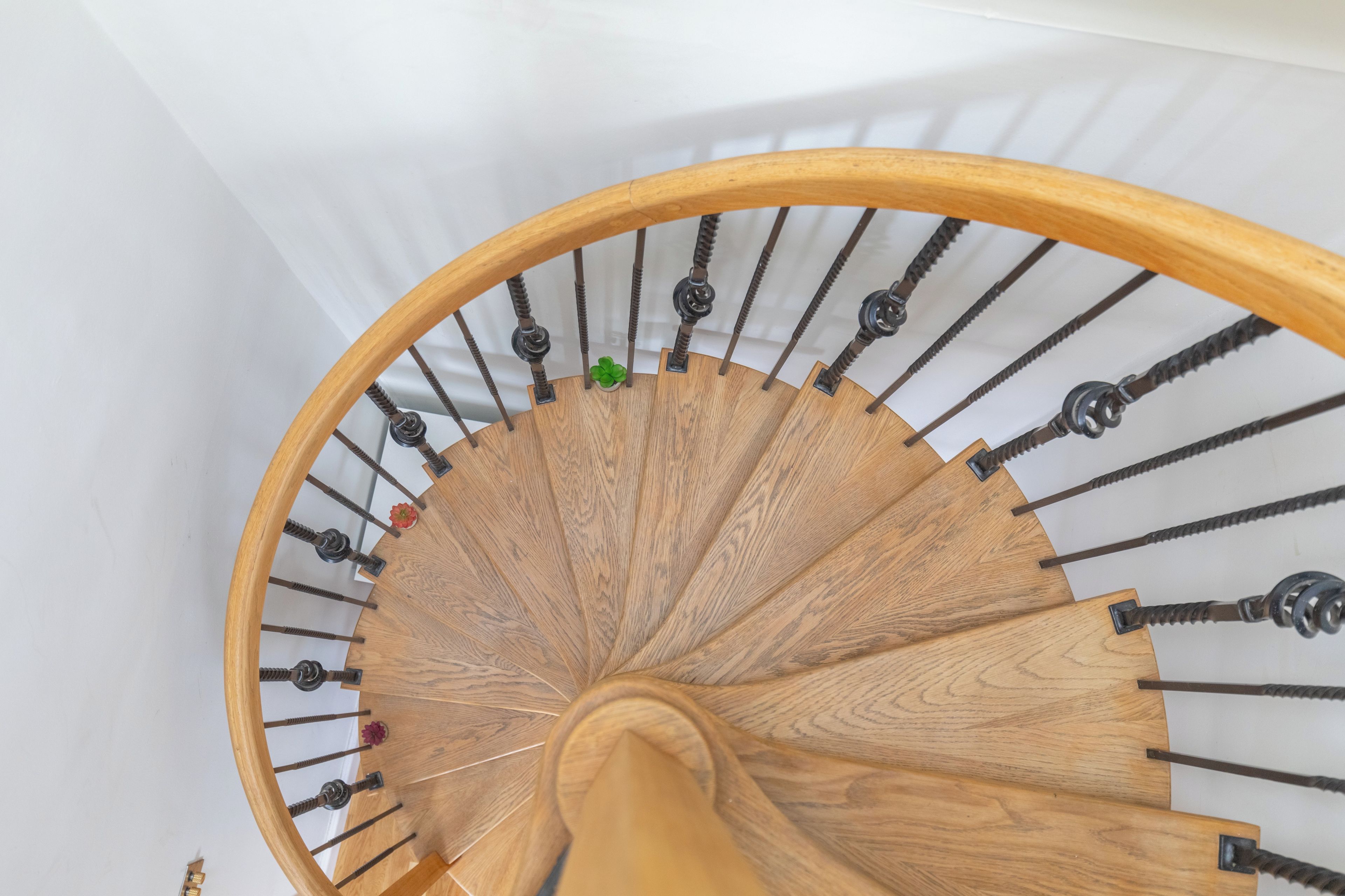 A wooden spiral staircase with metal balusters and a white wall background.